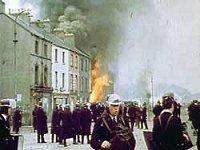 Image of policemen in riot gear in front of a burning house